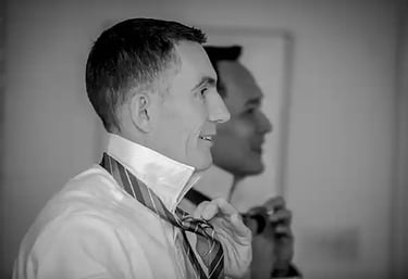 Black and white photo of two grooms tying their silk ties while getting ready for a wedding.