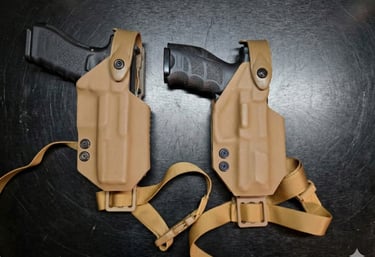 Two black handguns secured in tan kydex tactical holsters with nylon drop leg straps.