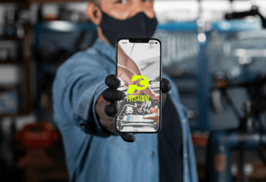 Auto mechanic holding a smartphone showing the Pitstopr mobile app for car repair services.