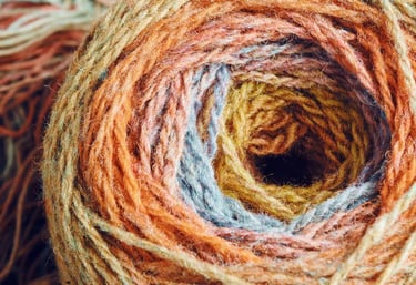 Primer plano de un ovillo de lana texturizada en tonos otoñales como naranja, dorado y azul.
