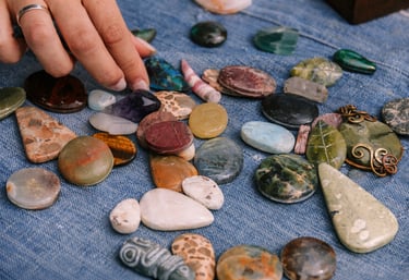 Mano seleccionando piedras naturales pulidas y minerales semipreciosos sobre tela de mezclilla azul para joyería artesanal.