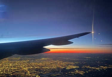 ala de avion en el cielo con vista a las luces de una ciudad y al atardecer naranja con azul 