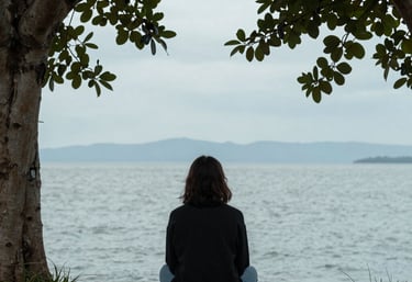 A woman sitting on a sofa, looking thoughtfully out the window, reflecting.