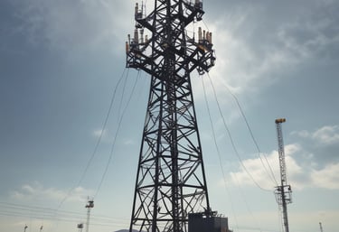 A team welding steel components for a towering transmission structure under a clear sky.
