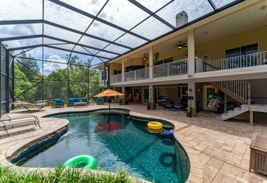 Luxury backyard swimming pool with a screen enclosure, patio furniture, and a balcony on a two-story home.