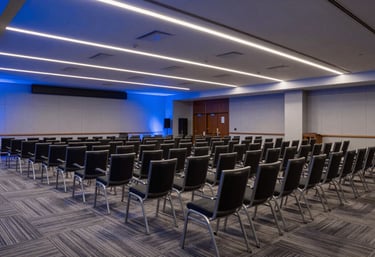 A wide shot of a modern conference hall in a North American / US city, rows of chairs, soft steel blue ambient lighting, clean and professional setup.