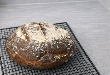 Freshly baked gluten-free artisan loaf bread cooling on a black wire rack atop a grey countertop.