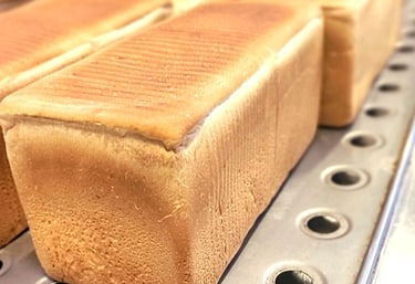 Freshly baked rectangular loaves of white sandwich bread cooling on a metal rack in a commercial bakery.
