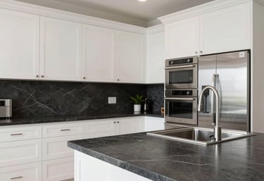 A high-end residential kitchen inside a North American luxury property. Features include clean white cabinetry, charcoal stone countertops, and stainless steel appliances. The lighting is bright and airy, suggesting quality and maintenance excellence.