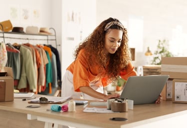 Female entrepreneur using a laptop to manage orders for her online clothing boutique shipping.