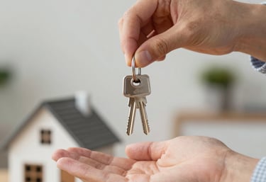 A person handing over house keys to a new homeowner with a model home in the background.