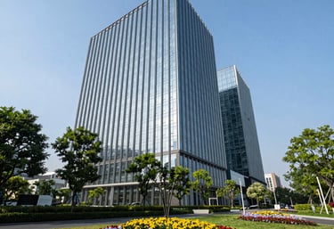 Low-angle photography of a sleek glass office building surrounded by healthy green parkland and flower beds, professional landscaping, clear blue sky.