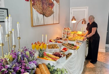 Buffet de catering profesional para eventos, fruta fresca, aperitivos, pasteles y decoración floral.