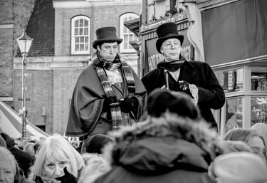 Performers in Victorian costumes with top hats and capes at a Dickensian Christmas festival.