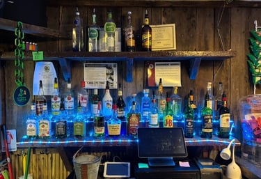 Rustic wood bar back shelf displaying various liquor bottles illuminated by blue LED lights.