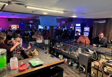 Crowded local bar with patrons, slot machines, and bartenders serving drinks in a dimly lit tavern.