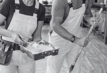 a man and woman in white overalls holding a paintbrush and paint roller