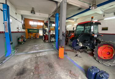 ένας μηχανικός τρακτέρ επισκευάζει ένα τρακτέρ με κουβούκλιο μέσα στο μεγάλο συνεργείο