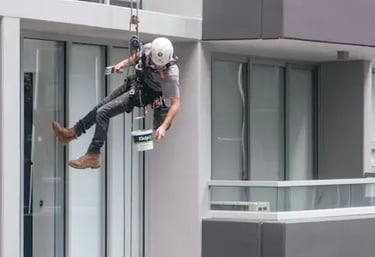 Artisan façadier de DM Rénovation effectuant un ravalement de façade sur cordes sur un immeuble à Landivisiau