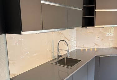 Cuisine moderne en L, meubles gris mats, plan de travail foncé et crédence effet marbre.