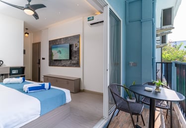 Modern hotel room with blue accents, flat-screen TV, and a private balcony with outdoor seating.