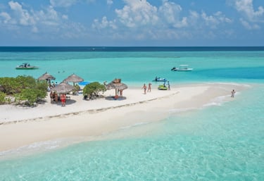 Aerial view of a tropical sandbar in the Maldives with thatched umbrellas and turquoise water.