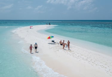 Aerial view of tourists relaxing on a white sandbar surrounded by turquoise ocean water in the Maldives.
