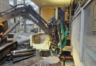 A Volvo excavator performs foundation drilling and piling at a modern urban construction site.
