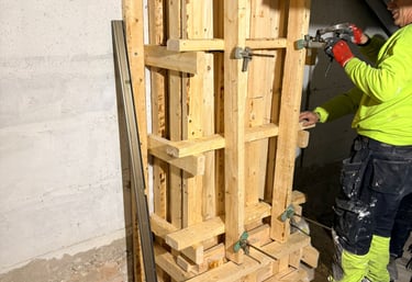 A construction worker securing a wooden concrete column formwork with clamps in a basement.