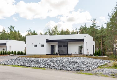 Modern white minimalist villa with a flat roof and stone landscaping surrounded by a pine forest.