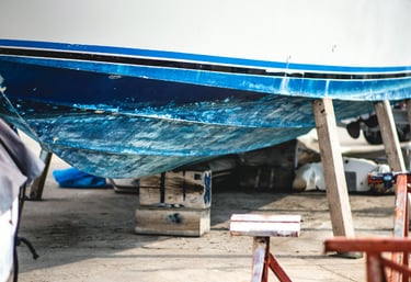 Close-up of a blue and white boat hull supported by wooden blocks for marine maintenance.