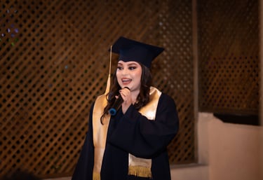 Una graduada sonriente con toga y birrete negros dando un discurso frente a un micrófono .