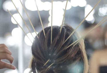Peluquero profesional peinando un elegante recogido castaño con palitos de bambú frente a un espejo 