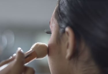 Maquilladora profesional aplicando polvos en el rostro de una mujer usando una brocha de contorno