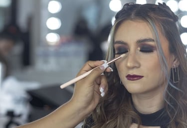 Maquilladora profesional aplica sombra de ojos ahumada oscura a una mujer en un estudio de belleza.