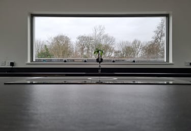 Modern kitchen sink with a chrome faucet in front of a large picture window overlooking a winter forest.