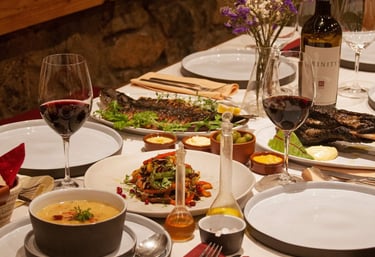 Gourmet dinner table with red wine, grilled fish, appetizers, and soup at a rustic restaurant.
