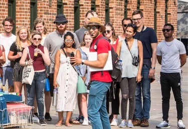 A tour guide in a red shirt leads a walking tour group in front of a historic brick building.