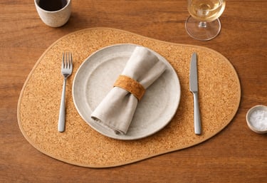 Minimalist table setting with a ceramic plate, linen napkin, and cork placemat on a wooden table.