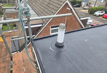 Flat roof installation with a white vent pipe and waterproof seal surrounded by scaffolding.
