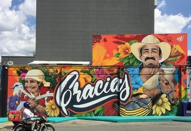 Vibrant outdoor street art mural featuring Latin American figures, flowers, and the word Gracias.