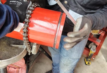 A plumber uses a metal file to smooth the edge of a red PVC pipe secured by a chain vise tool.
