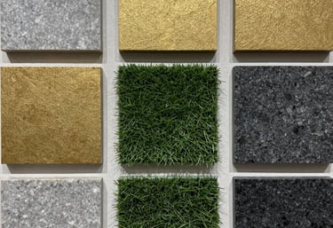 A high-quality physical presentation board showcasing luxurious material samples: grey travertine pavers, textured gold claddings, synthetic turf fibers, and dark charcoal granite cubes, arranged in a neat architectural grid.