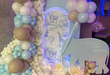A baby shower decoration features a blue elephant cutout with 'Rachael's Baby Shower' text, surrounded by white, blue, and