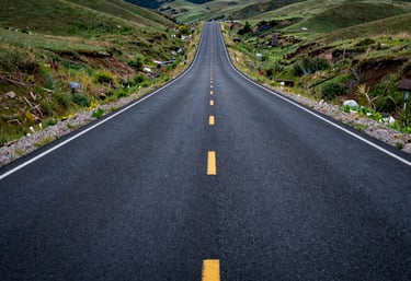 A wide-angle landscape shot of a newly paved asphalt road stretching into the distance through green hills, North American / US location.
