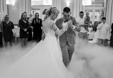 Black and white photo of a bride and groom dancing on a floor covered in low fog during their wedding reception.