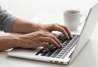 Hands typing on a sleek laptop keyboard in a bright Sul-Americano / Brasileiro environment, with a coffee mug and a clean white background.