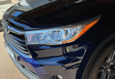 Close-up of a blue Toyota SUV headlight and front bumper in a driveway.