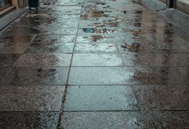A close-up of clean, power-washed stone pavement in a Central European / German commercial courtyard. The stones are wet, reflecting the Muted Teal sky. No weeds, perfectly maintained.