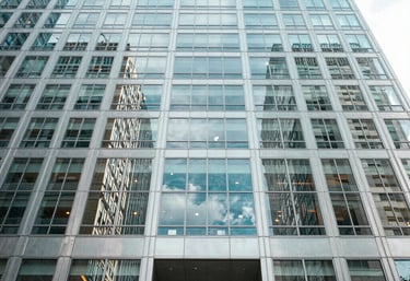An architectural shot of a glass-and-steel skyscraper lobby in the United States. The perspective is looking up, conveying authority with light blue and white tones.